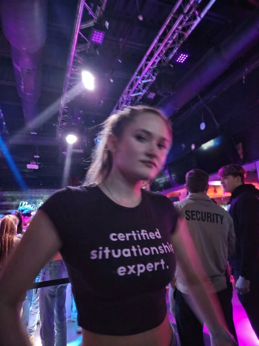 Woman at a club wearing a black Sparkbite baby tee that reads "certified situationship expert."